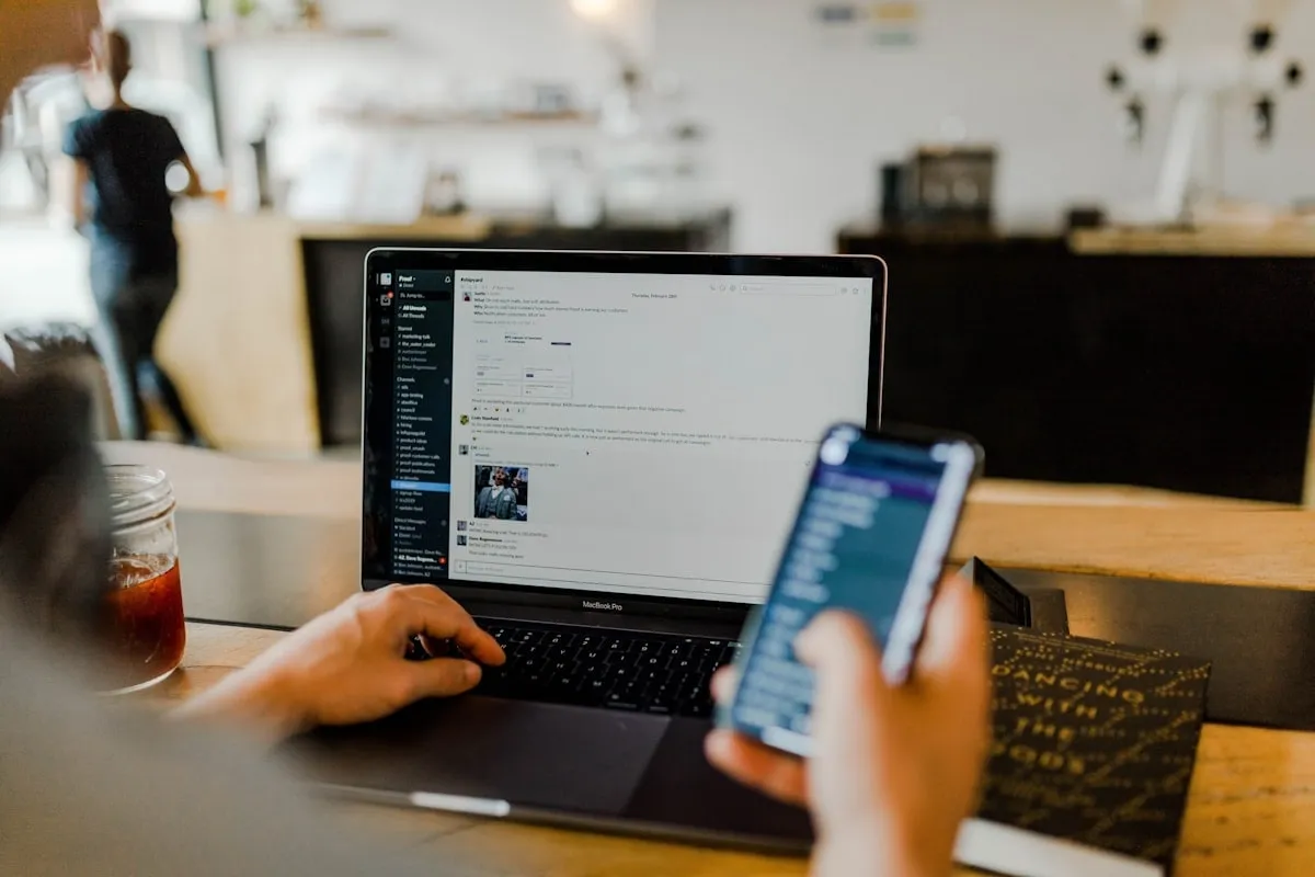 Collaborateur consultant un message sur son téléphone à côté de son ordinateur